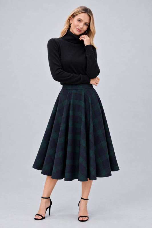 A woman modeling a black long-sleeve mock neck top and a dark green and black plaid pleated midi skirt, paired with black high-heeled sandals, against a solid light gray studio background.